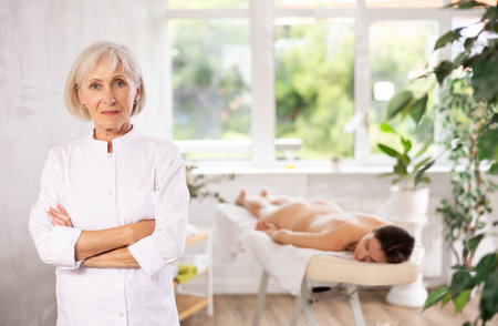 Female elderly physiotherapist poses against background of spa salons office.の写真素材