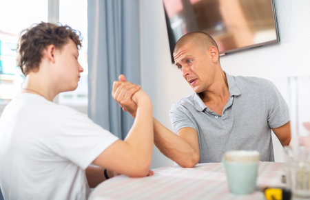 Happy smiling father and son arm wrestling at homeの写真素材