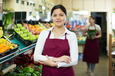Friendly woman vegetable shop seller posing behind counterの写真素材
