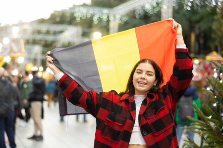 Smiling girl with flag of Belgium walking on street Christmas fairの写真素材