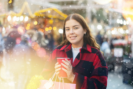 Girl with paper cup of tea walking at street Christmas fairの写真素材