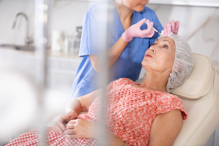 Female doctor gives injection of botulinum toxin to elderly woman patient in foreheadの写真素材