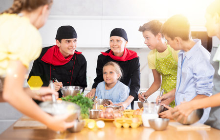 At cooking lesson, male cook in black suit tells children about cuisine, woman assistant helps childの写真素材