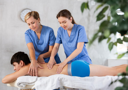 Young masseuse trainee with experienced female mentor doing back massage to manの写真素材