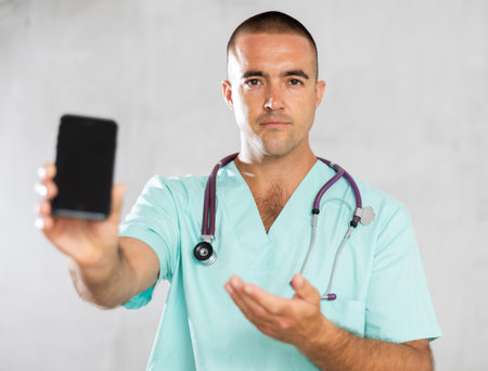 Male doctor in medical uniform posing with mobile phone in medical roomの写真素材