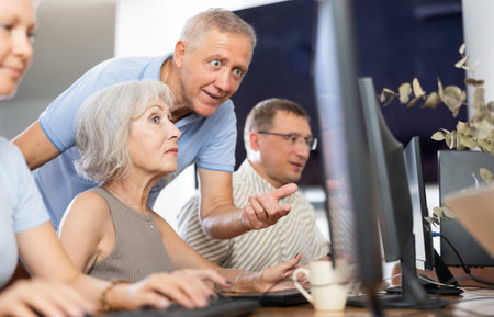 Friendly elderly computer course teacher helping woman learn computerの写真素材