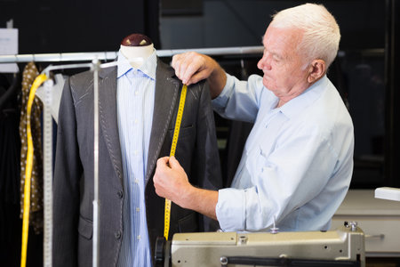 Mature male tailor takes measurement from his jacket using measuring tapeの写真素材
