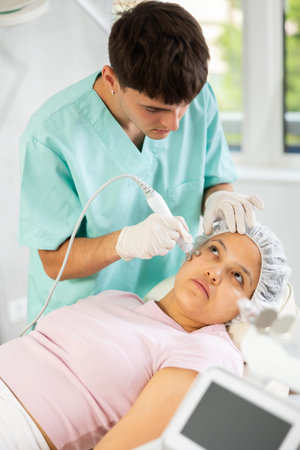 Young male cosmetologist doing microcurrent procedure to young woman