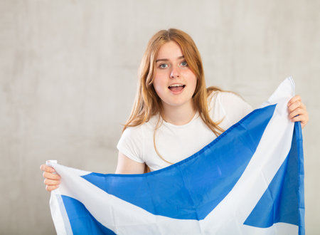 smiling girl in arms raised above head holds cloth of national flag of Scotlandの写真素材