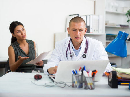 Doctor writing prescription to female patient on laptop at clinicの写真素材