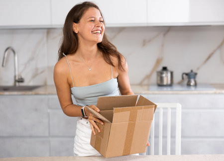 Young smiling woman holding open box in kitchen
