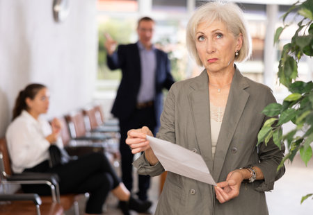 Upset elderly woman with documents standing in receptionの写真素材