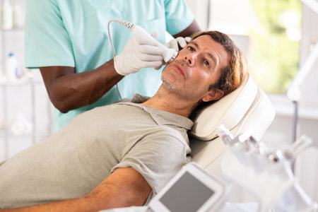 African male specialist uses ultrasonic import nozzle to care man client face skinの写真素材