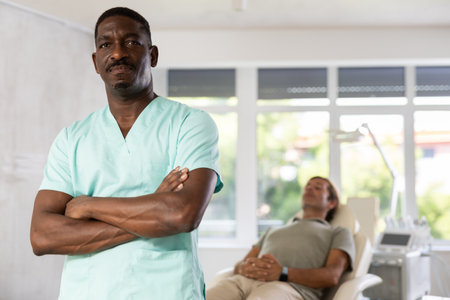 Middle-aged African man doctor stands with arms crossed on chest in hospital officeの写真素材