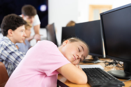 Tired female schoolgirl fell asleep on computer keyboard in class