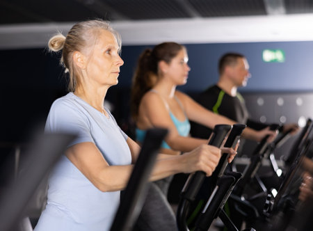 Mature woman exercising on an elliptical trainer in gym