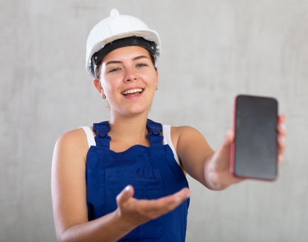 Young woman in work overalls posing with phoneの写真素材