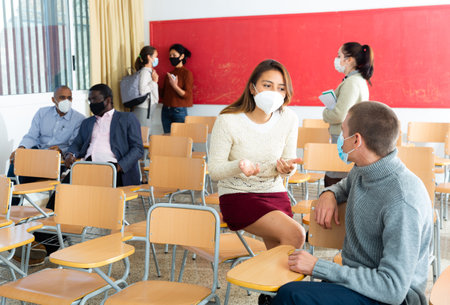 Students in protective masks are talking about homework at deskの写真素材