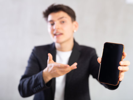 Surprised young guy holding mobile phone in his handの写真素材