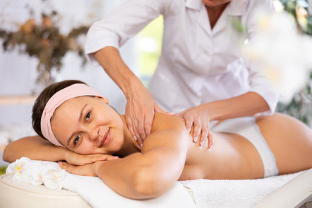 Female masseur works out shoulder and back problem area for female athlete client. Close-upの写真素材