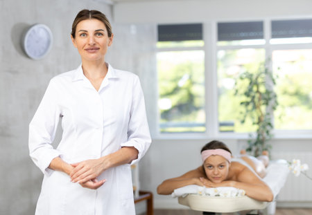 Positive young professional masseuse standing in massage roomの写真素材