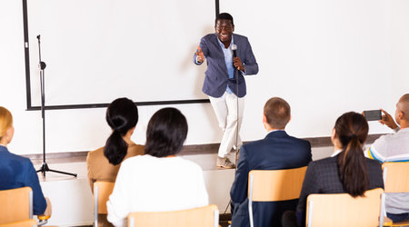 Expressive african american speaker with microphone on conference room stageの写真素材