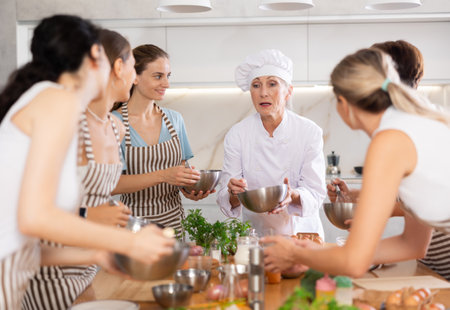 Elderly woman chef with bowl in hands tells women at culinary courses about traditions of cuisineの写真素材