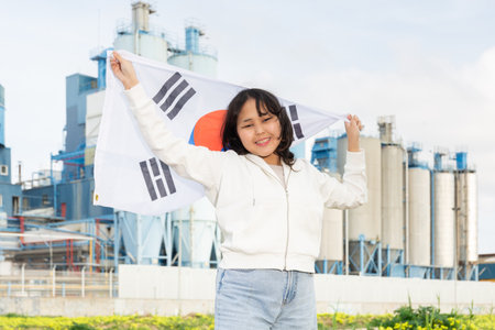 Portrait of teenage girl with flag of South Korea in her hands against the backdrop of modern metallurgical plantの写真素材