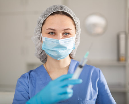 Young female nurse in a protective mask prepared a syringe with medicine for injectionの写真素材