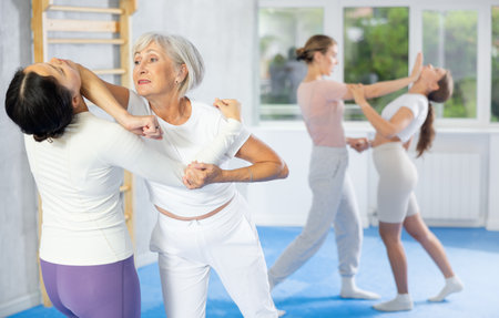 Elderly woman performing armlock with elbow strike to chin during training sparring in self-defense trainingの写真素材