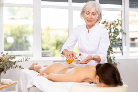 Professional masseuse applying oil to hands to make back massage to womanの写真素材