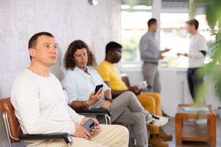 Middle-aged male visitor sitting on chair in waiting hall of clinic