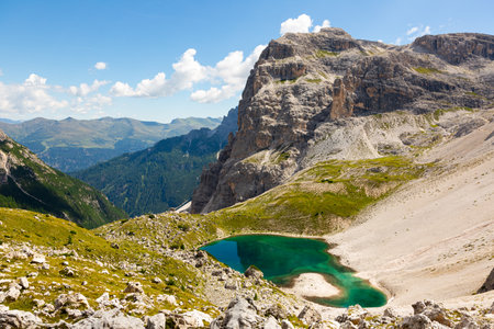 White sandy-rocky slope descends to shore of small lake in Laghi dei piani area with emerald waterの写真素材