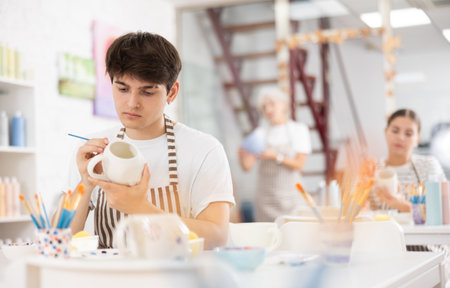 Focused guy enthusiastically painting on ceramic cup in pottery classの写真素材