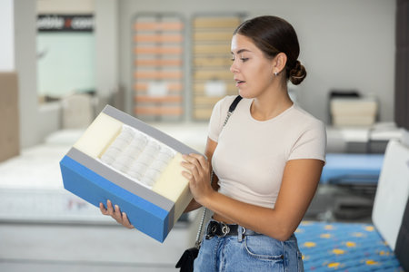 Girl examines samples structure of spring mattress in furniture store.の写真素材