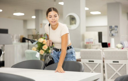 Interested young girl choosing dining table in furniture storeの写真素材