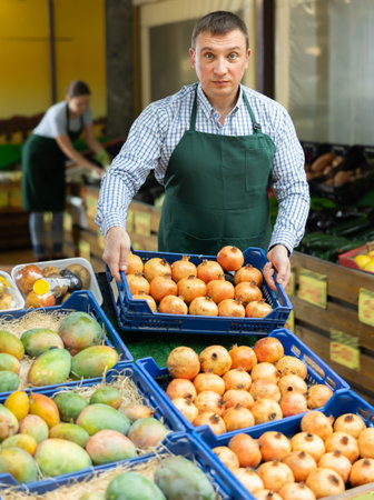 Green grocery store owner arranging plastic boxes with pomegranates on counterの写真素材