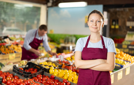 Positive and friendly store woman employee stands with arms crossed on chest and waits for customersの写真素材