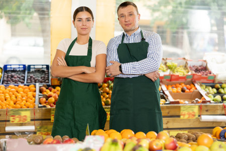 Smiling father and daughter, owners of green grocery store, standing among stalls of fruits and vegetablesの写真素材
