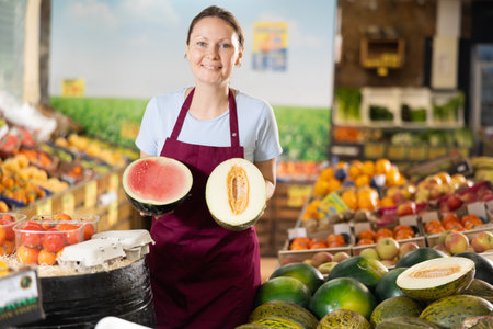 Woman grocery store seller offers a choice of buying ripe melon or watermelon.の写真素材
