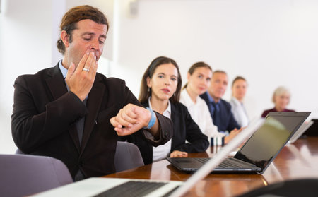 Businessman looking at wristwatch at business meeting in meeting roomの写真素材