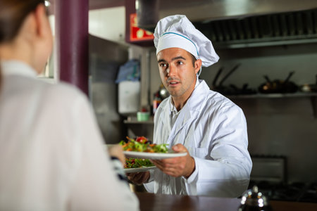 Service process in cafe - chef serves ready meals to visitors of modern restaurant