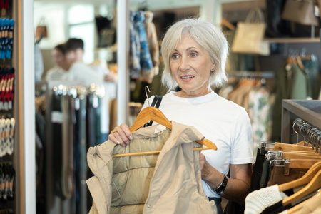 Old woman choosing beige vest in clothing storeの写真素材