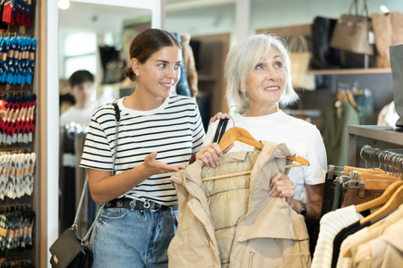Girl lay heads together with old woman friend about purchasing vest during shoppingの写真素材