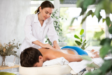 Young woman performs back shoulder massage to male client.の写真素材