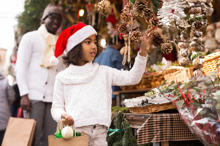 Girl with toy in hand choosing decorations at Christmas marketの写真素材