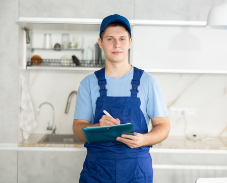 Young maintenance worker noting down cleaning tasks in home kitchenの写真素材
