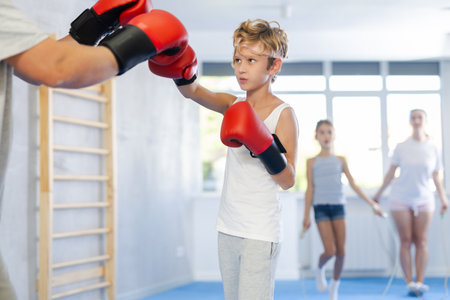 Boy with her trainer father at gym. Boy wearing boxing gloves exercise and punch to pads for boxingの写真素材