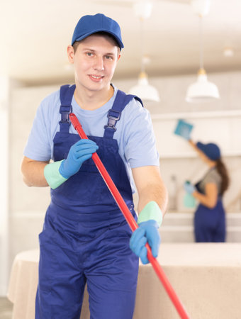 Guy employee of cleaning company in blue jumpsuit cleans and washes floor in kitchenの写真素材