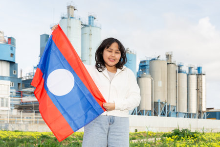 Happy young woman with flag of Laos against background of factoryの写真素材